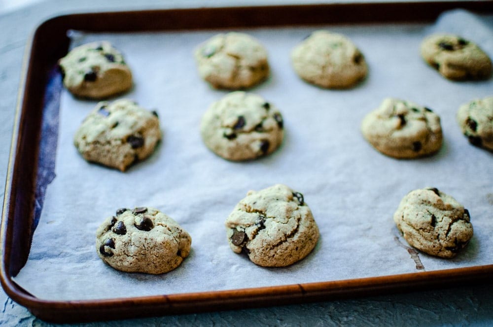 A baking tray with twelve sorghum flour chocolate chip cookies rests on parchment paper.