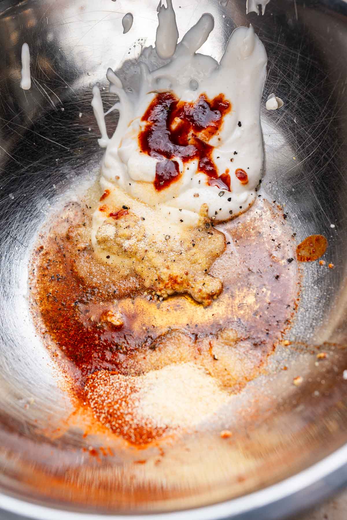 A stainless steel bowl holds a zesty cajun coleslaw mix with mayonnaise, soy sauce, chili paste, black pepper, and spices.
