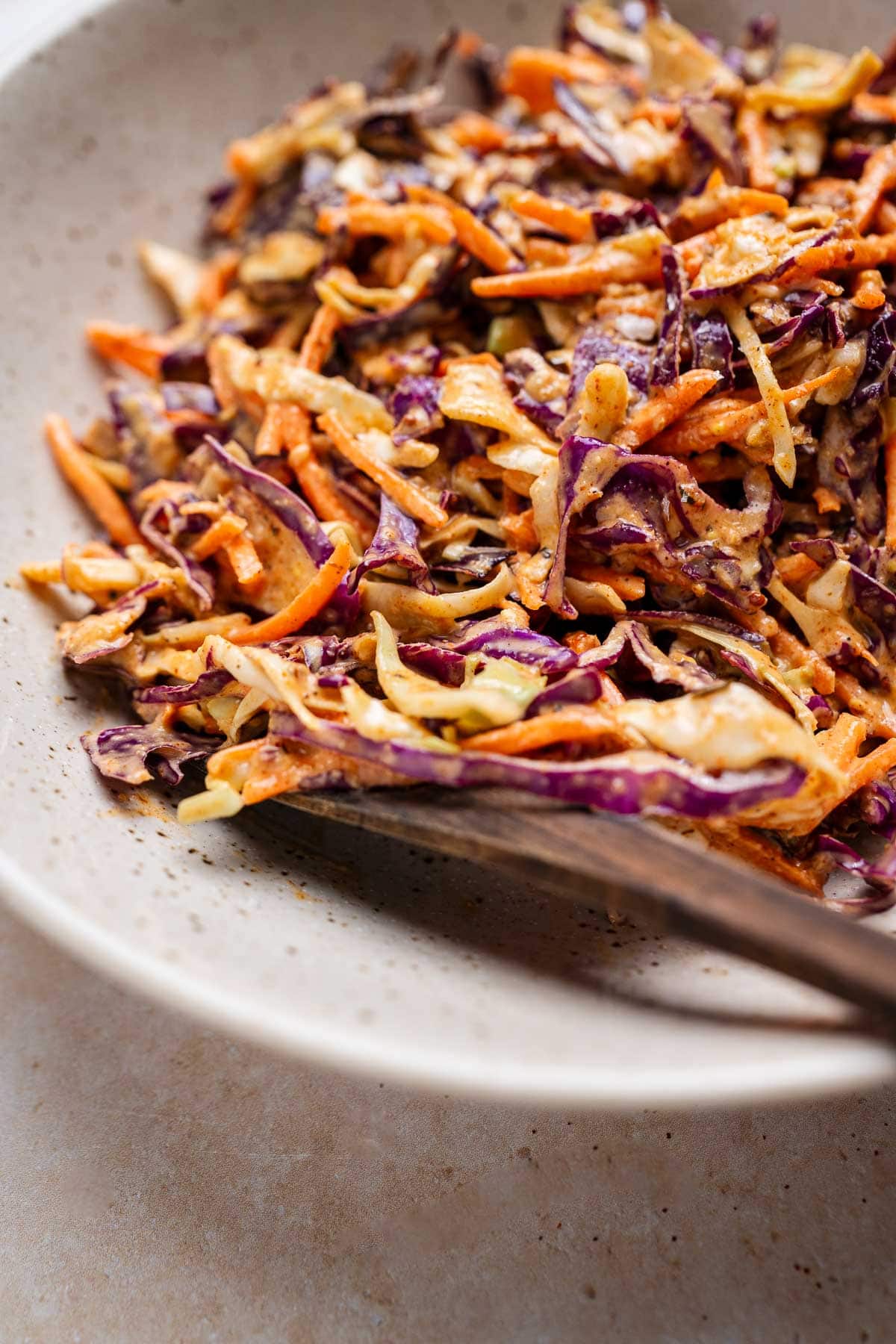 A bowl of Cajun coleslaw featuring shredded purple and green cabbage, and carrots, all mixed with a creamy dressing infused with a hint of spicy southern flair.