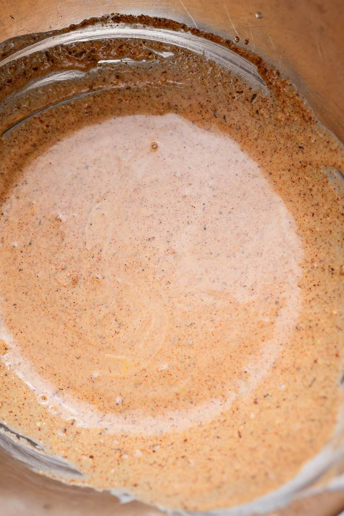 A close-up of a cajun coleslaw-style brown and white swirled batter or mixture in a metal bowl.