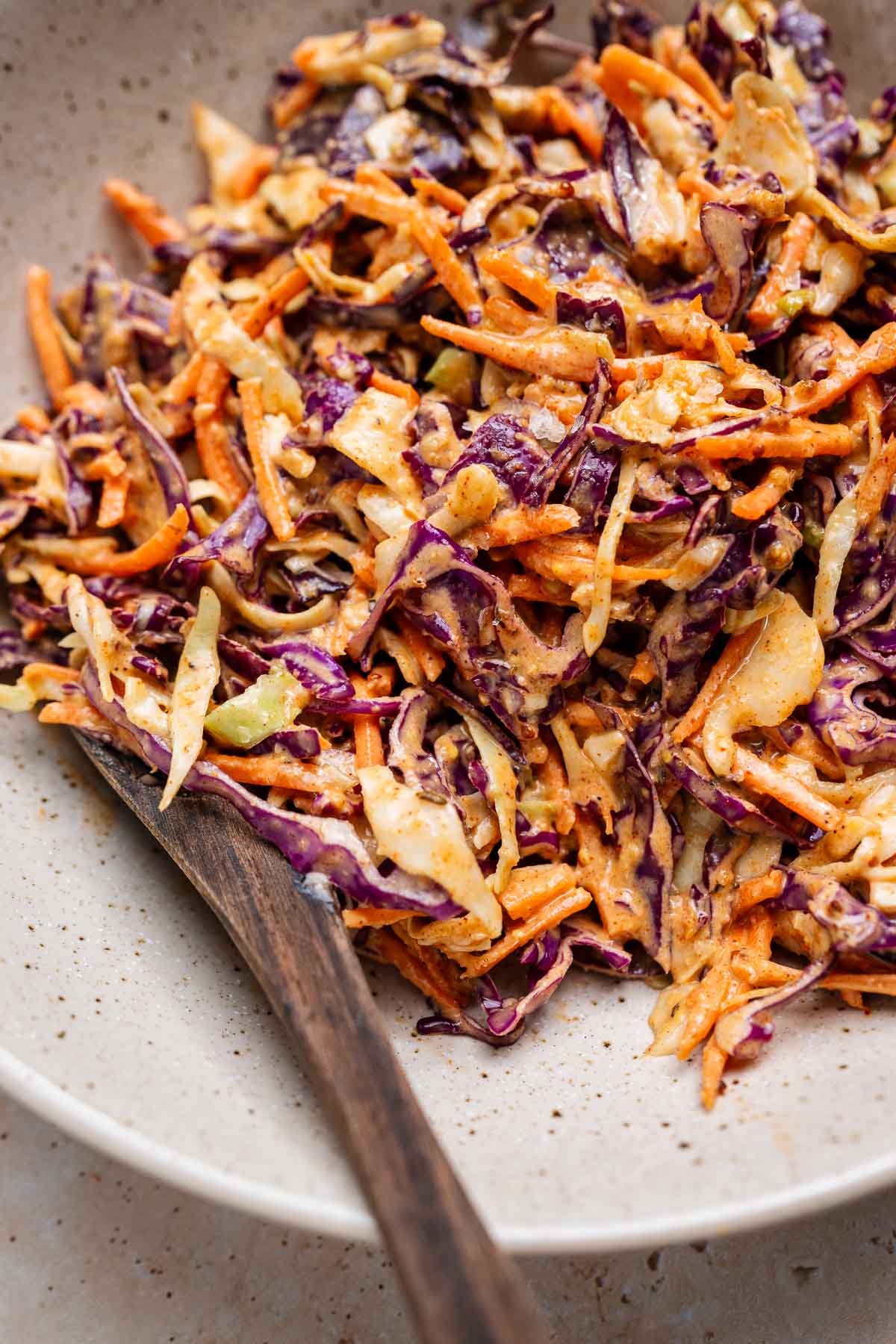 A bowl of vibrant Cajun coleslaw with shredded carrots, purple and green cabbage, melded with a zesty creamy dressing, and accompanied by a wooden spoon.