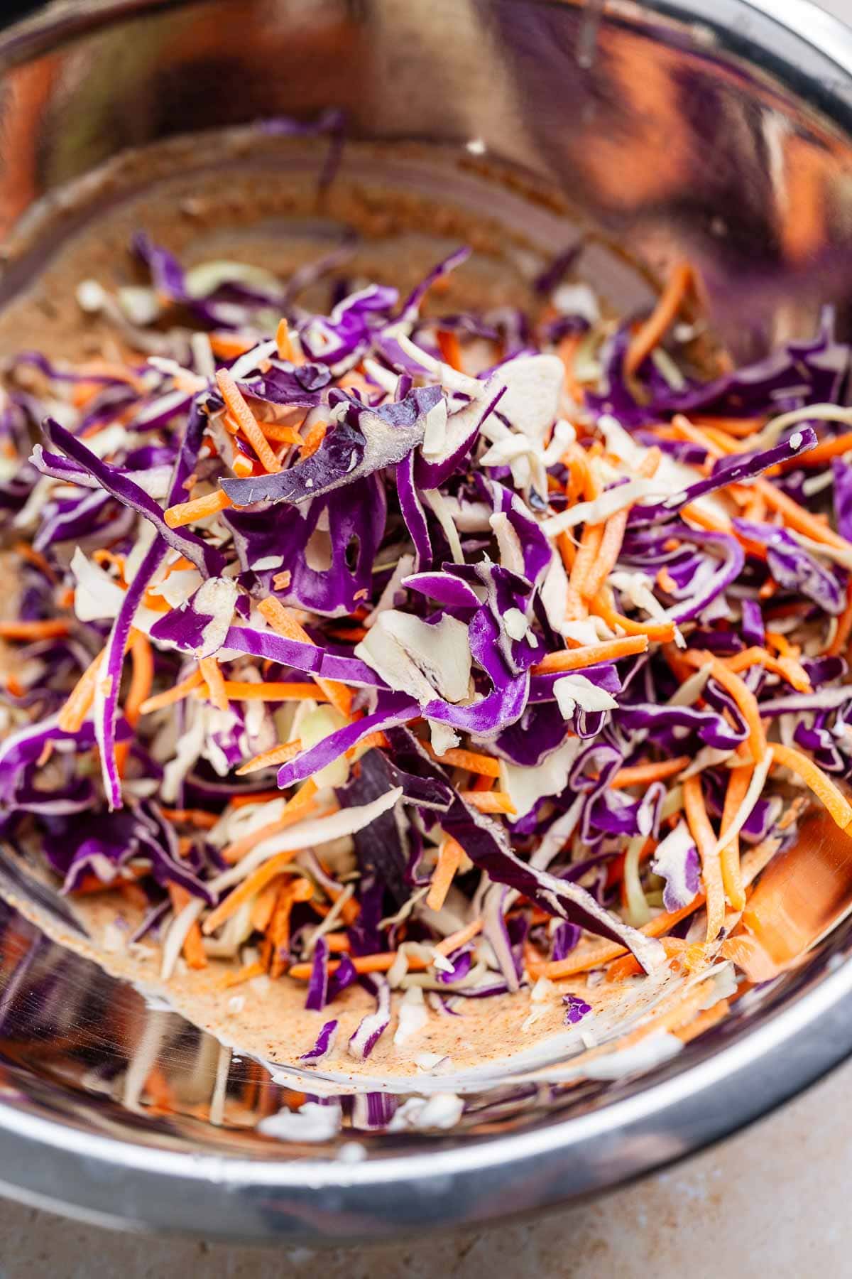 Bowl containing a zesty cajun coleslaw mix of shredded purple cabbage, carrots, and cabbage.