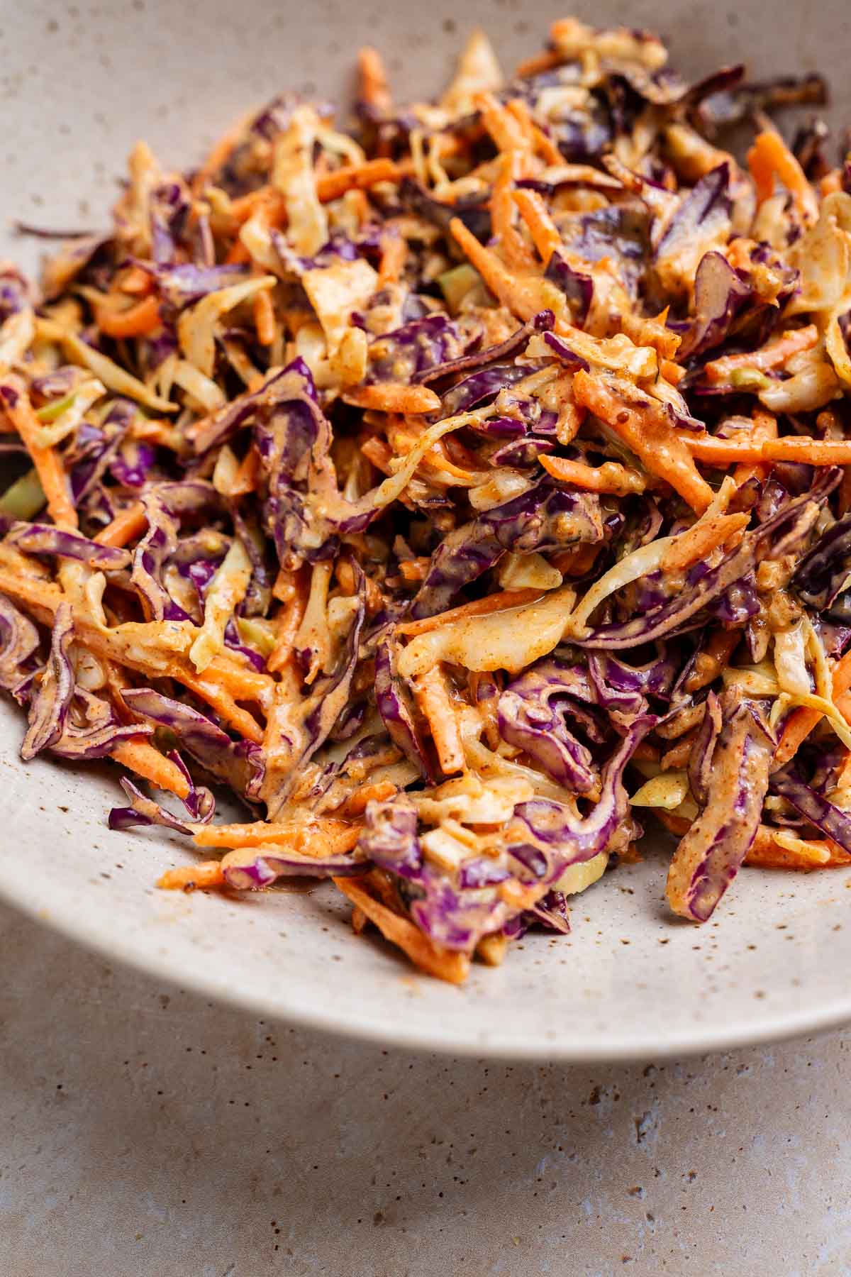 Close-up of a bowl filled with vibrant cajun coleslaw, featuring shredded purple and green cabbage, and carrots, all lightly coated in a creamy dressing.