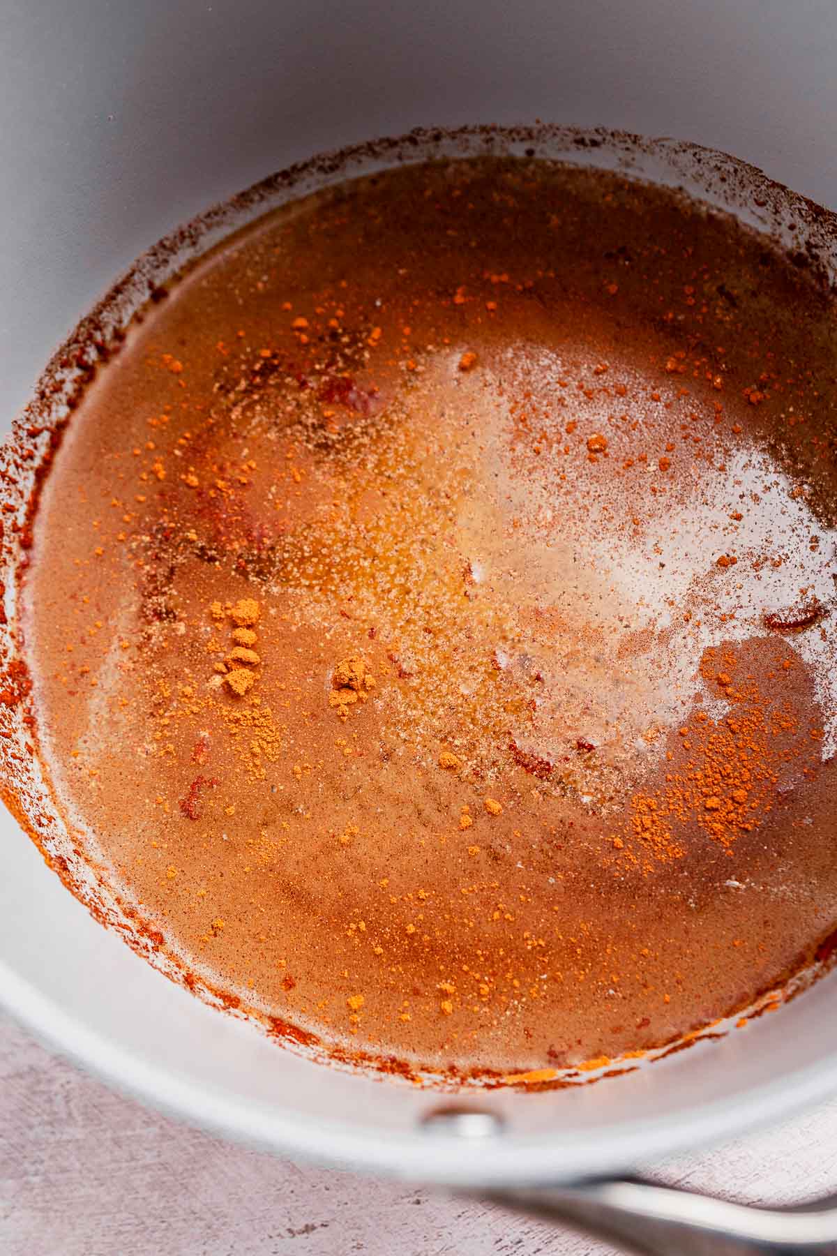 A white pot containing a frothy chai coffee mixture with visible spices and a rich brown hue.
