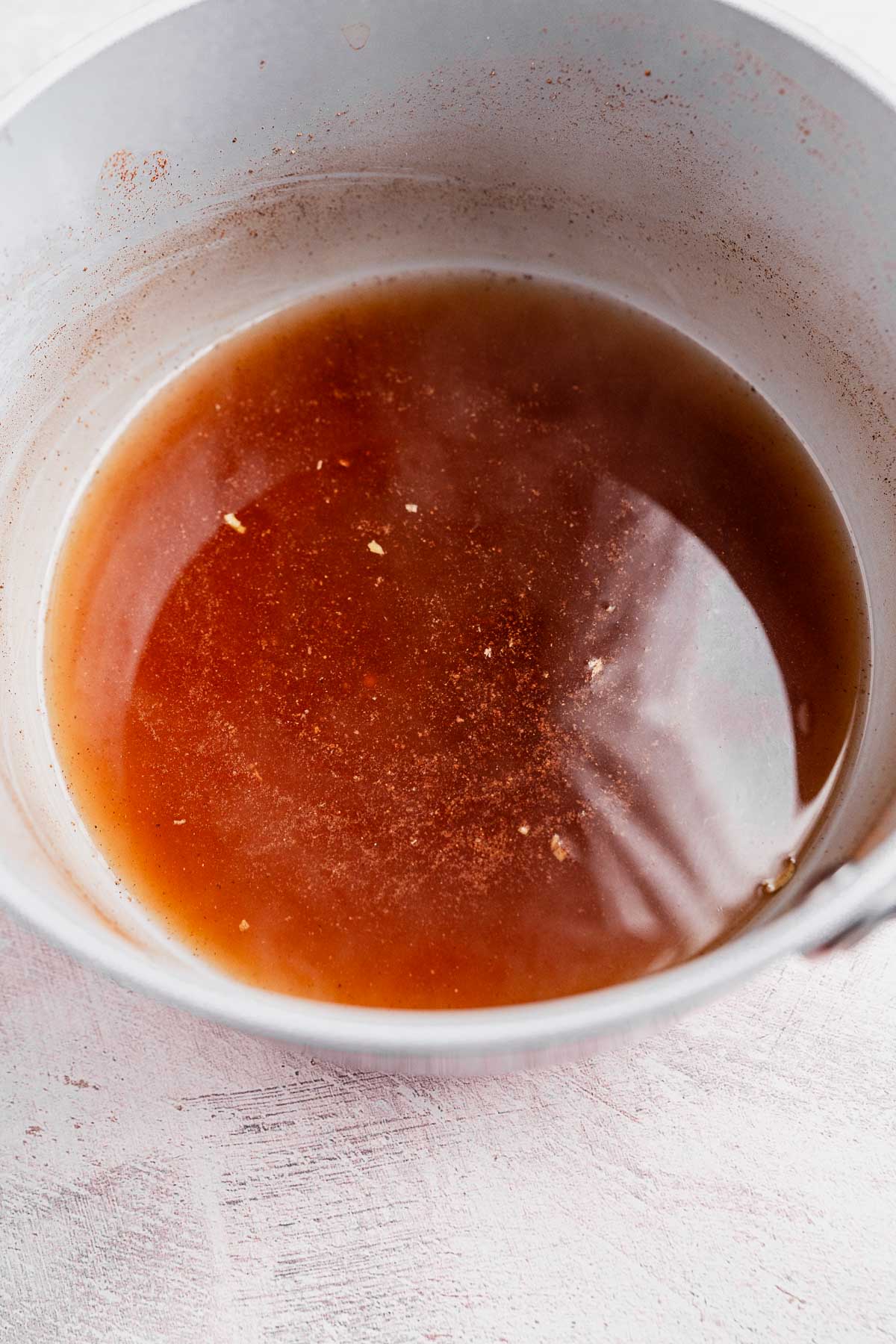 A bowl containing a rich, brown chai liquid with some small particles, set on a light-colored surface.