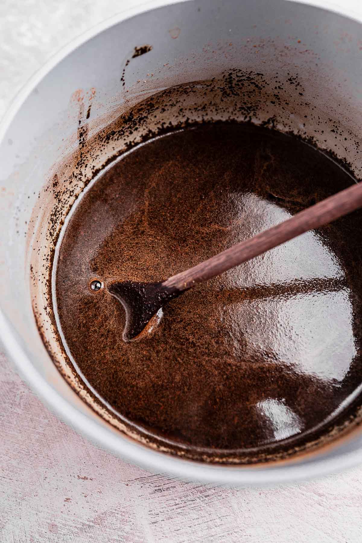 A mixing bowl containing a rich, dark brown chai coffee concoction swirls as a wooden spoon stirs the aromatic contents.