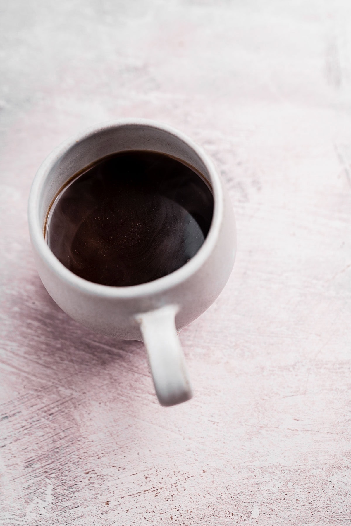 A steaming cup of chai coffee in a white ceramic mug, resting on a light textured surface.