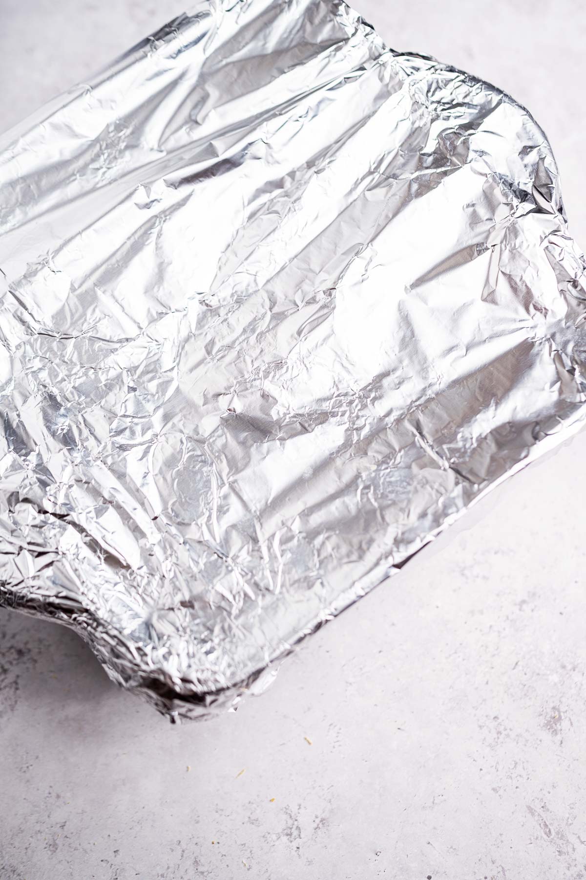 A baking pan covered with crumpled aluminum foil holds the promise of mouthwatering cheese enchiladas casserole, all set against a light gray surface.