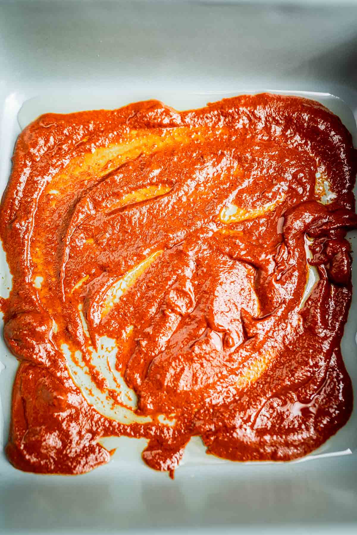 A spread of red enchilada sauce blankets the surface of a cheese enchiladas casserole in the baking dish.