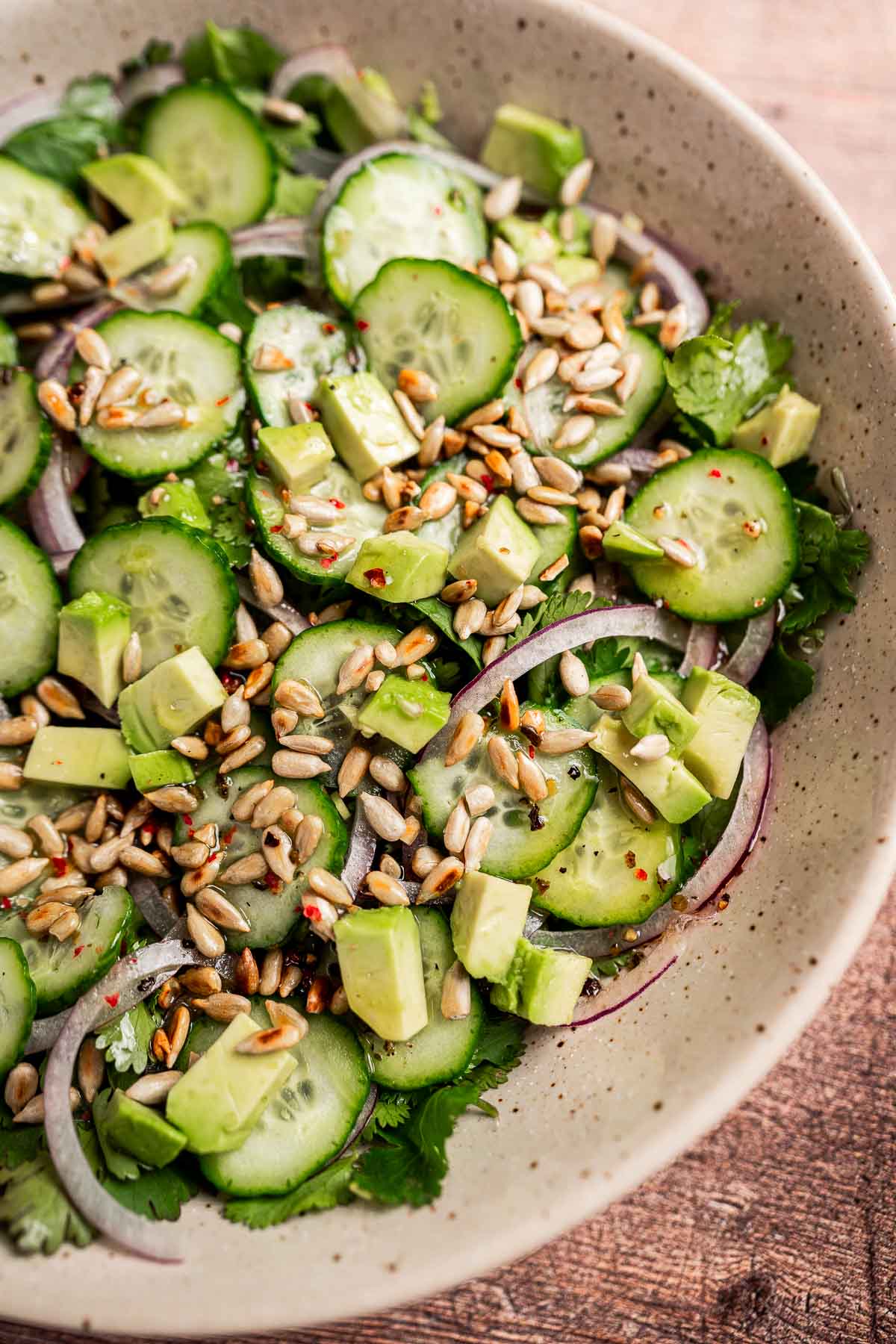 A cilantro salad featuring a vibrant mix of sliced cucumber, red onion, creamy avocado cubes, and crunchy sunflower seeds combines fresh flavors into one delightful bowl.