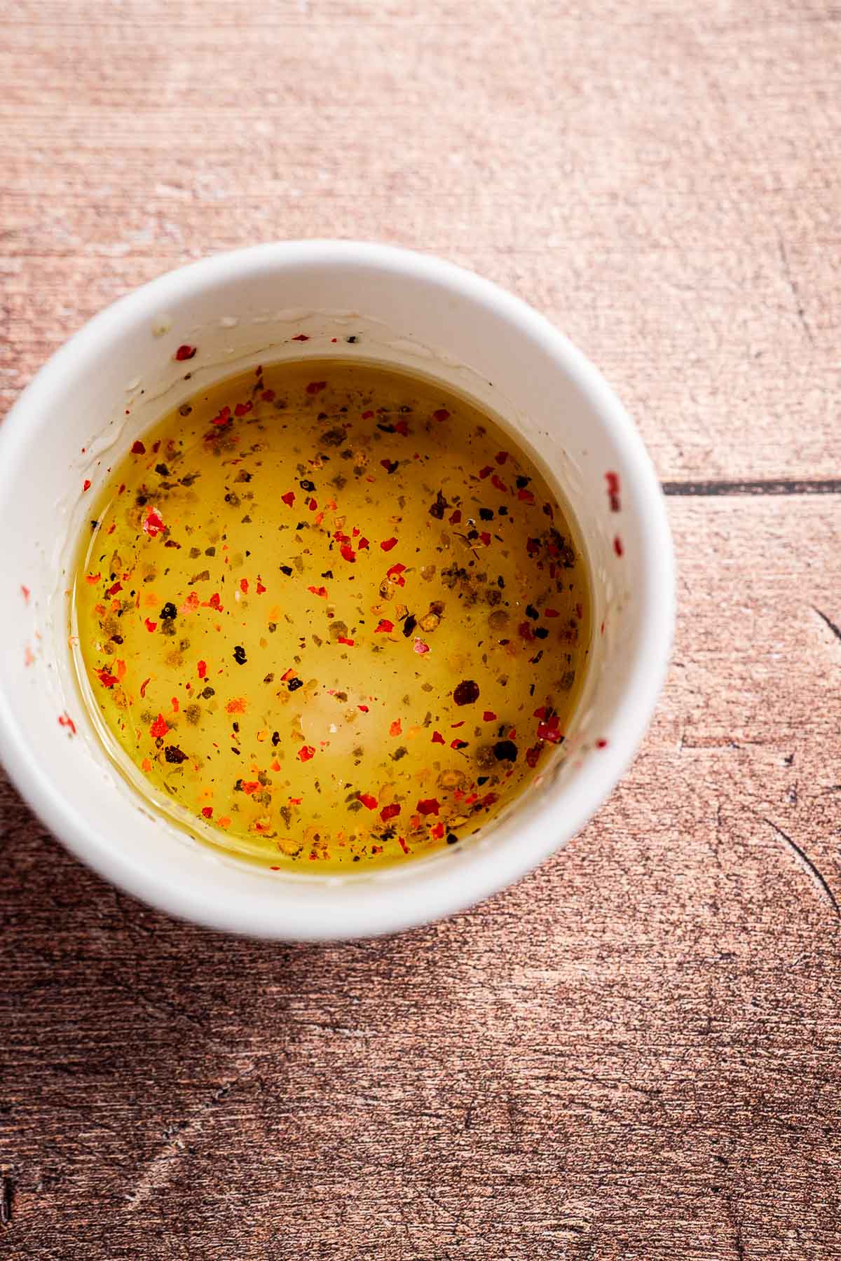 A white bowl filled with seasoned olive oil, containing red pepper flakes and herbs, sits on a wooden surface, reminiscent of vibrant cilantro salad notes.