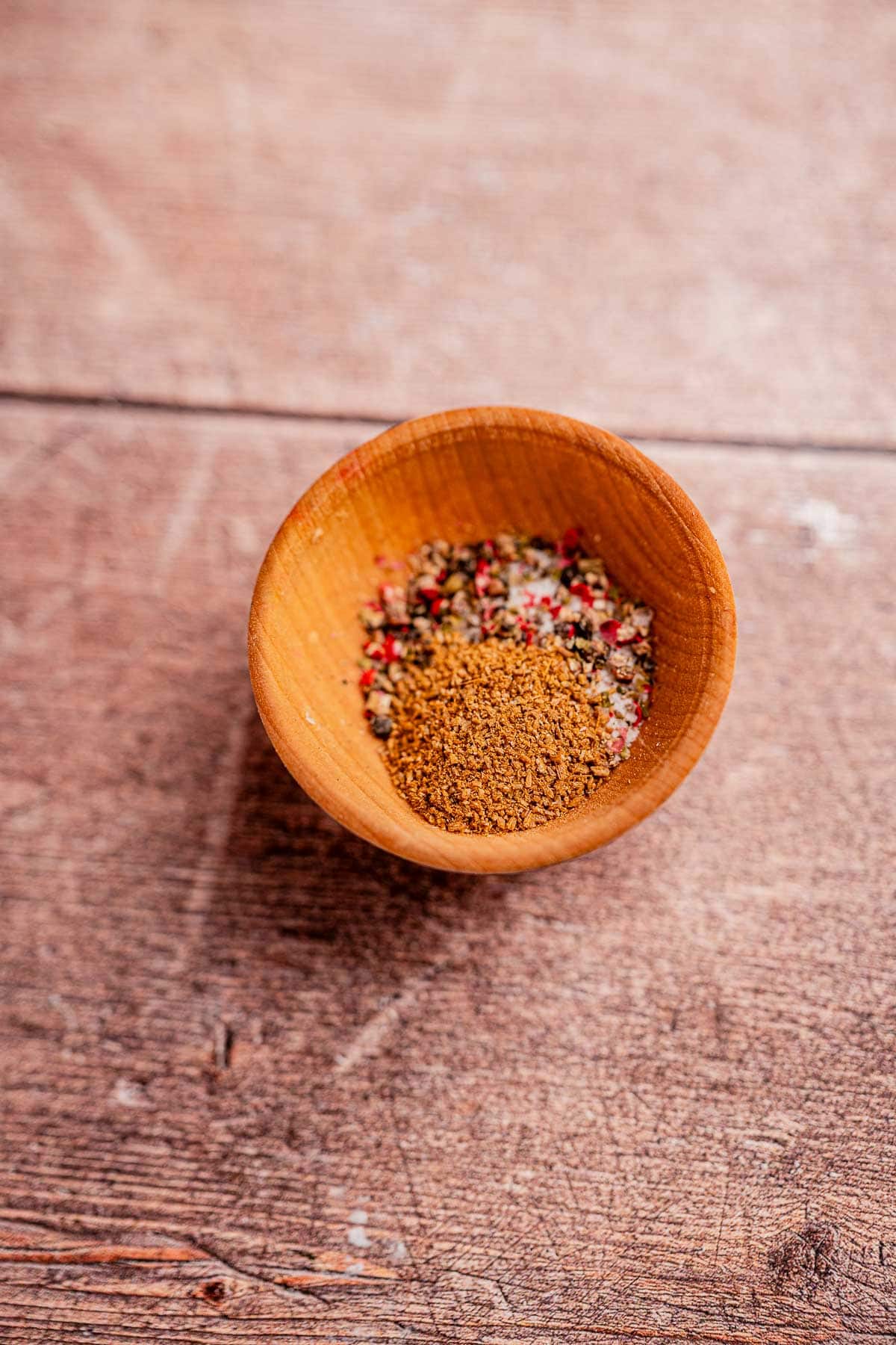 A small wooden bowl containing a mixture of various spices, including the rich flavors of hogao, sits on a wooden surface.