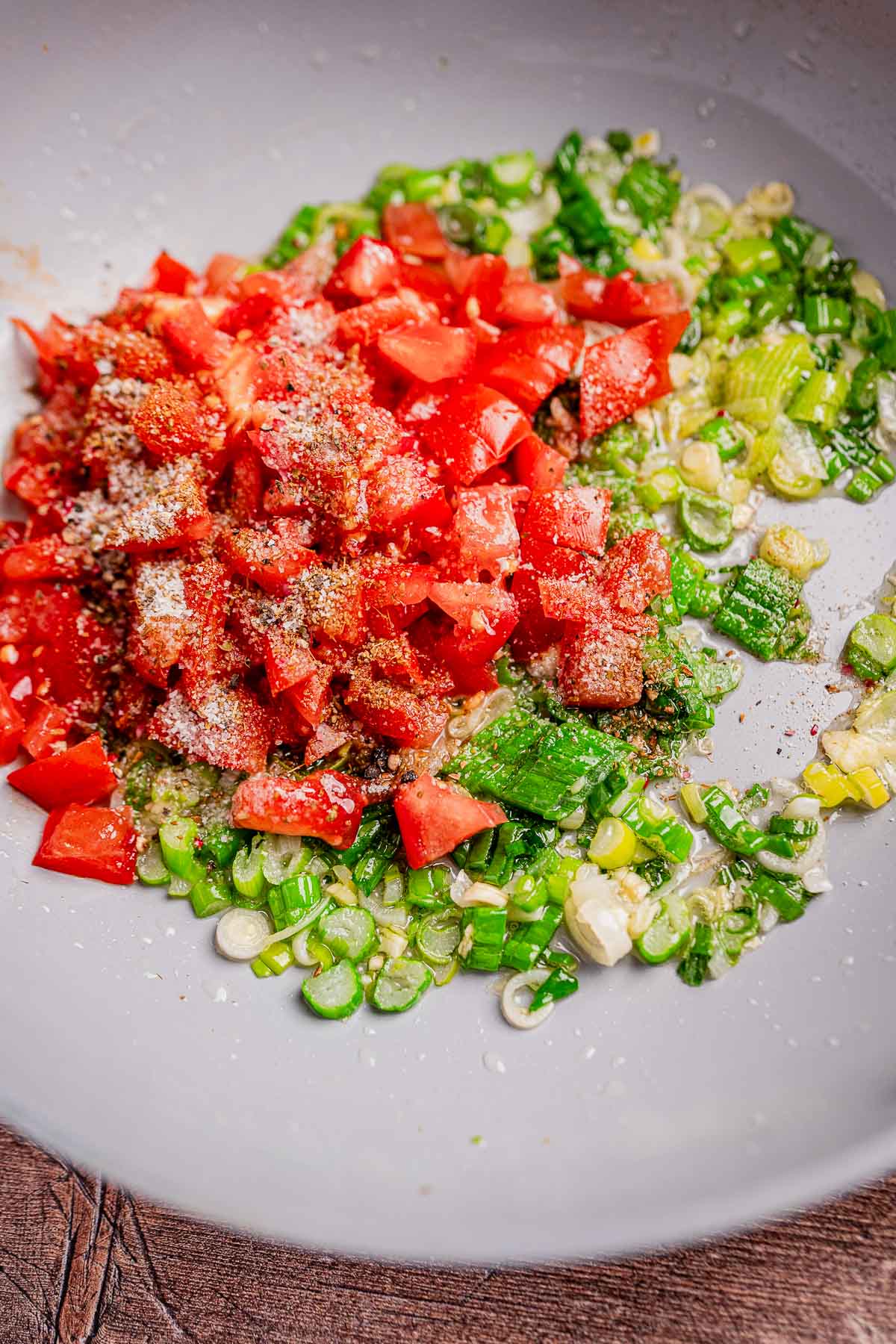 A white bowl brimming with chopped tomatoes and green onions, seasoned with salt, pepper, and a hint of hogao for a delightful twist.