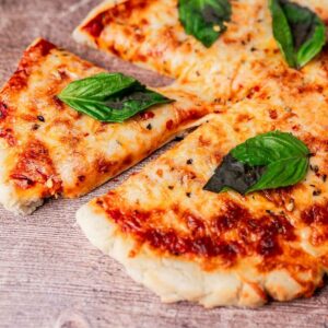 Close-up of a sliced pizza with melted cheese, tomato sauce, and fresh basil leaves on a wooden surface.