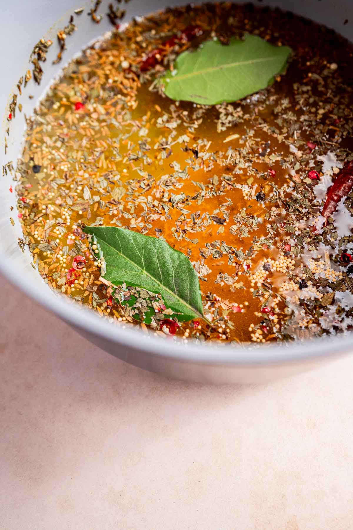 A bowl filled with seasoned broth, featuring two bay leaves, herbs, spices, and a hint of torshi floating on the surface.