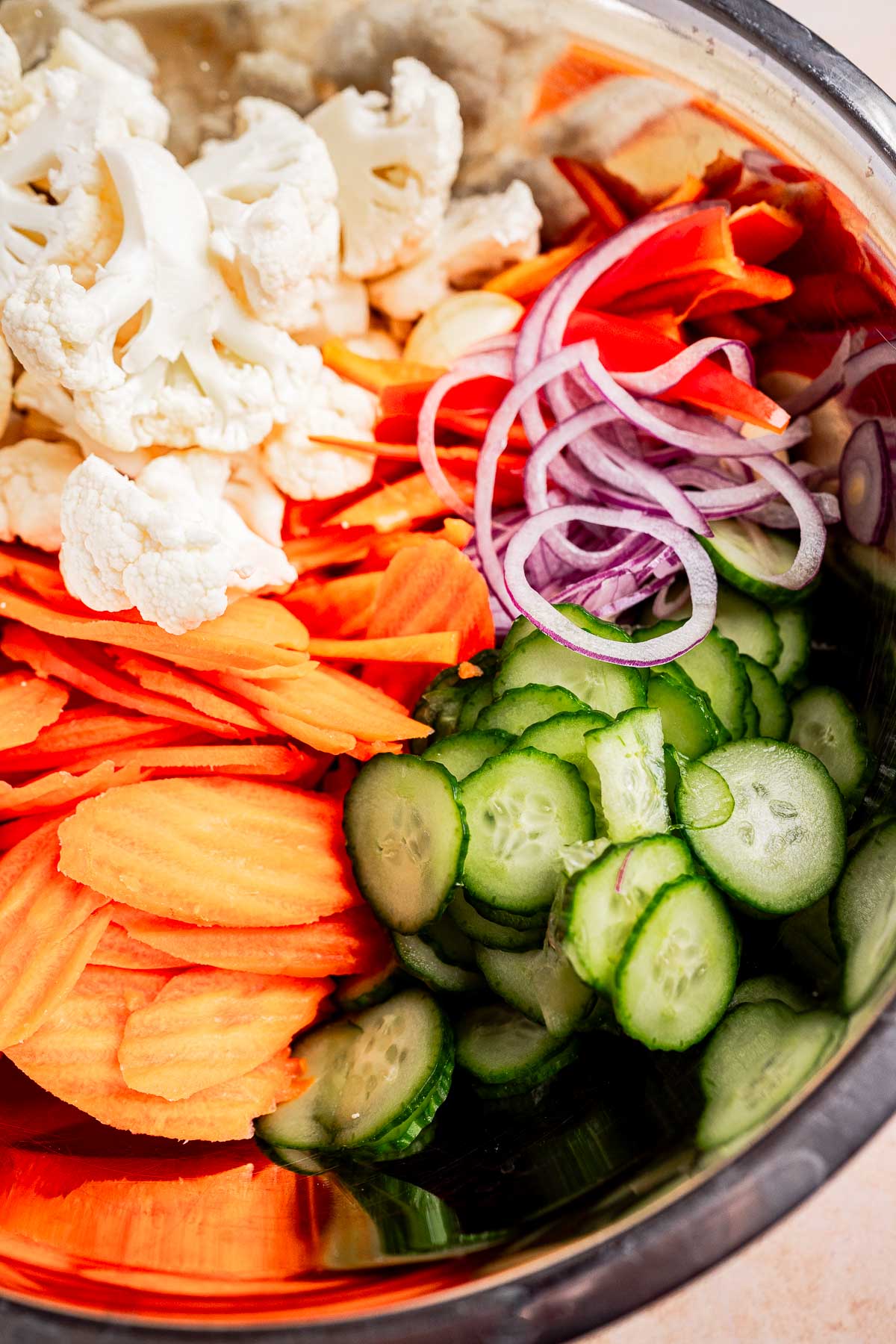 A bowl of torshi featuring sliced vegetables like cauliflower, carrots, red onions, and cucumbers.