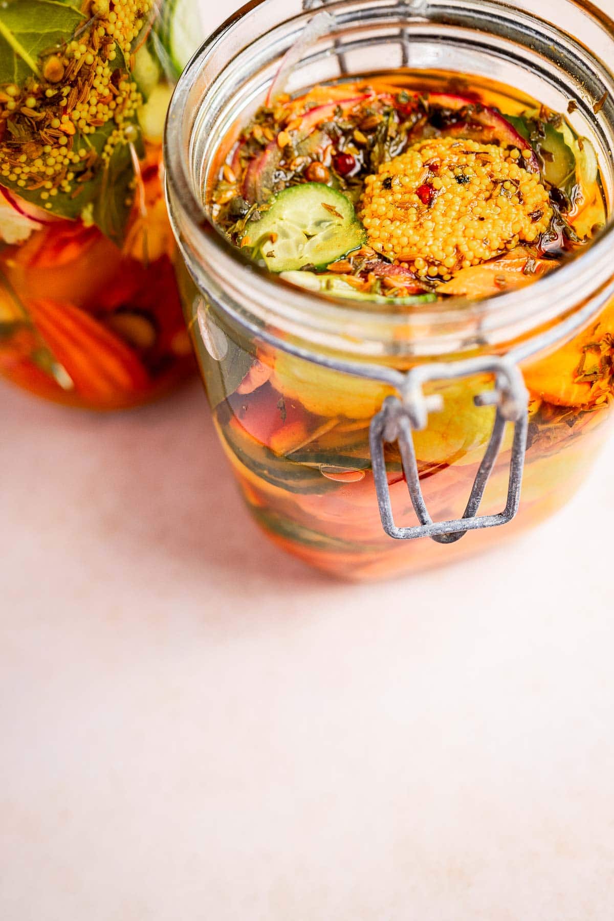 A glass jar brimming with torshi, a medley of mixed pickled vegetables like cucumbers, carrots, and aromatic spices, rests on a light surface.