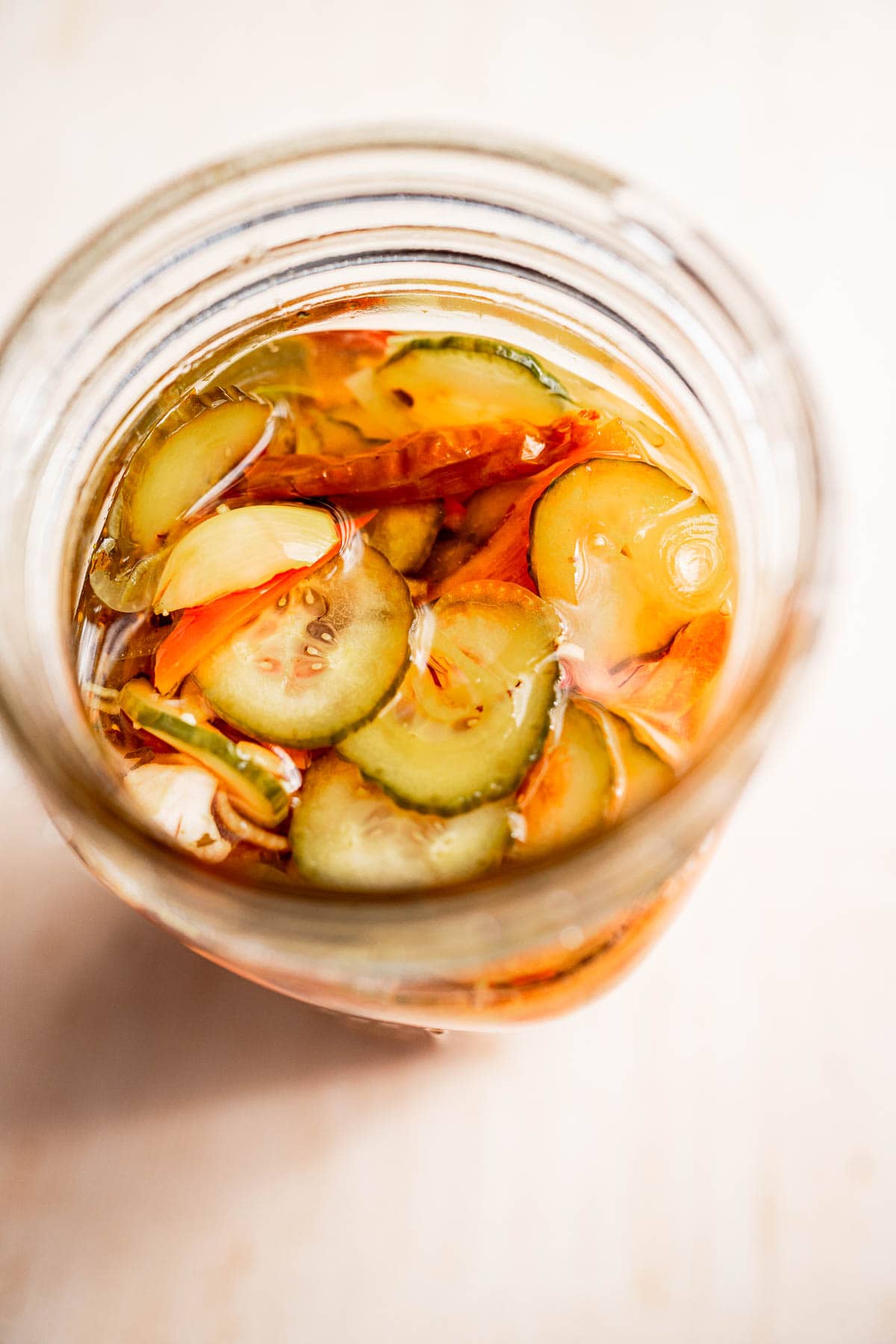 A jar of torshi, featuring an assortment of pickled vegetables like sliced cucumbers and peppers, is beautifully displayed from above on a light surface.