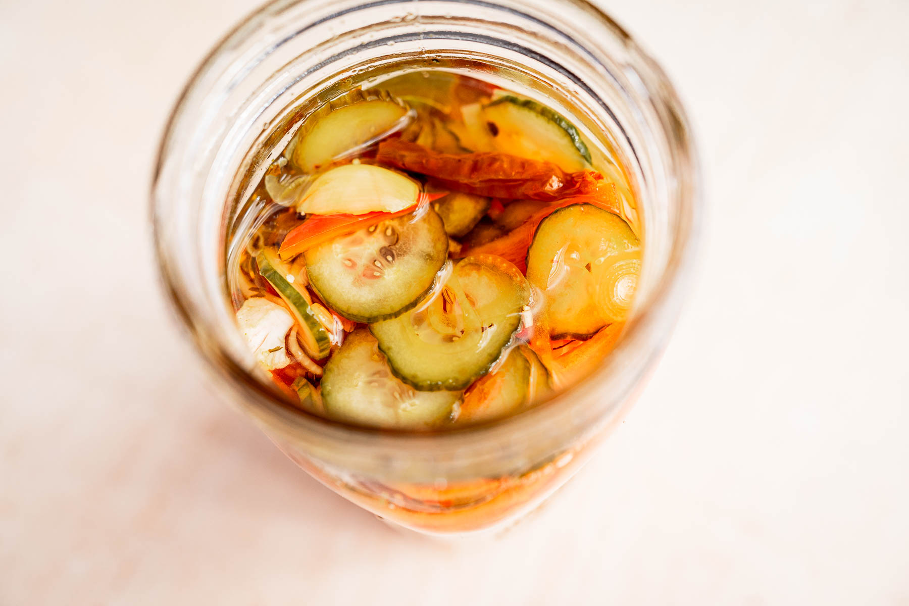 A glass jar brimming with torshi, featuring sliced cucumbers, carrots, and red peppers all submerged in a tangy vinegar-based liquid.