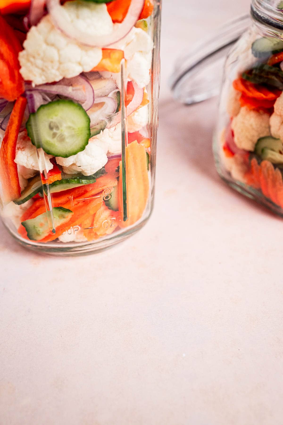 Jars brimming with torshi, a delightful mix of sliced cucumbers, cauliflower, carrots, and onions, rest elegantly on a light surface.