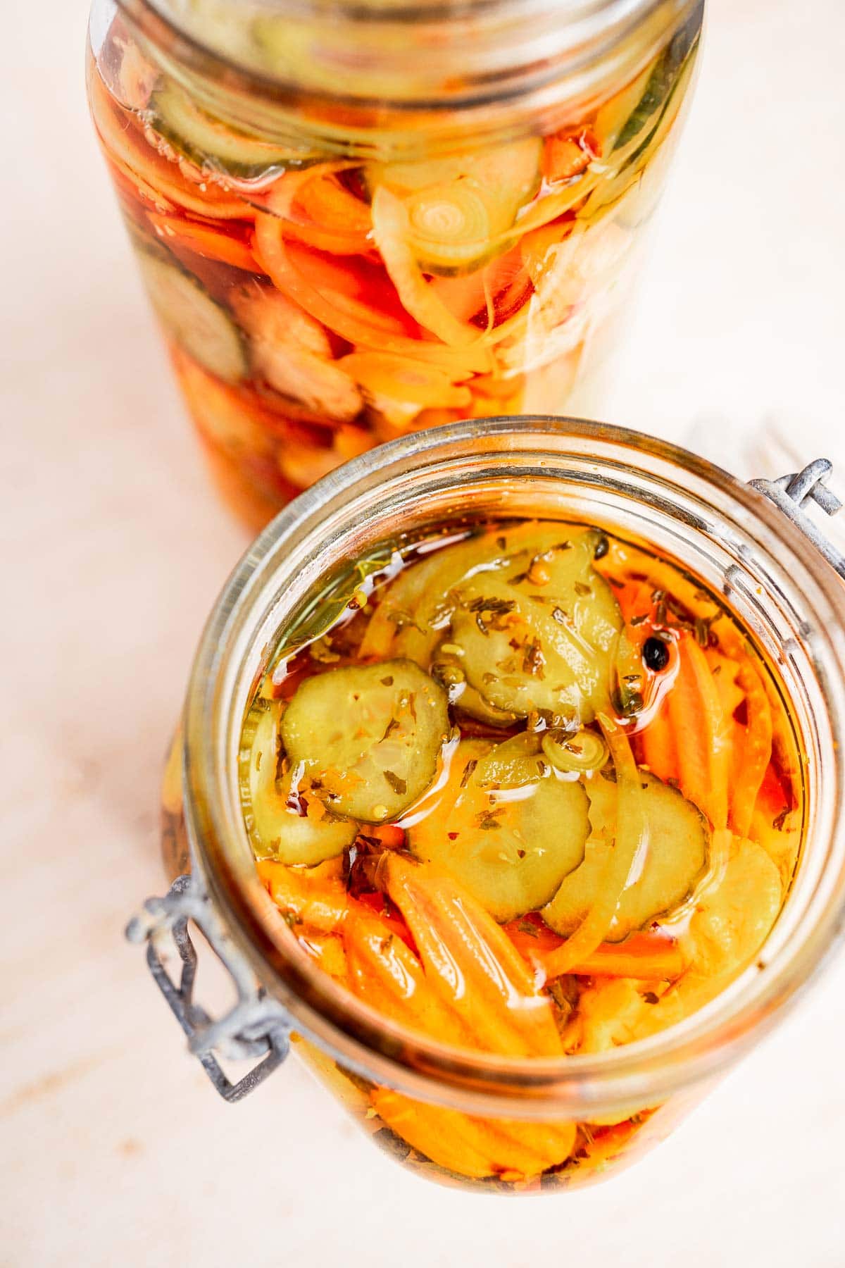 Two glass jars filled with torshi, featuring a colorful mix of sliced pickles, carrots, and onions in a tangy brine, viewed from above.
