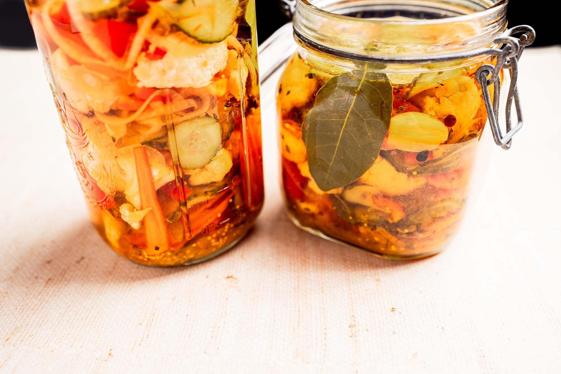 Two glass jars brimming with torshi—a delightful mix of vegetable pickles—sitting in a tangy liquid, accented by visible herbs and spices.