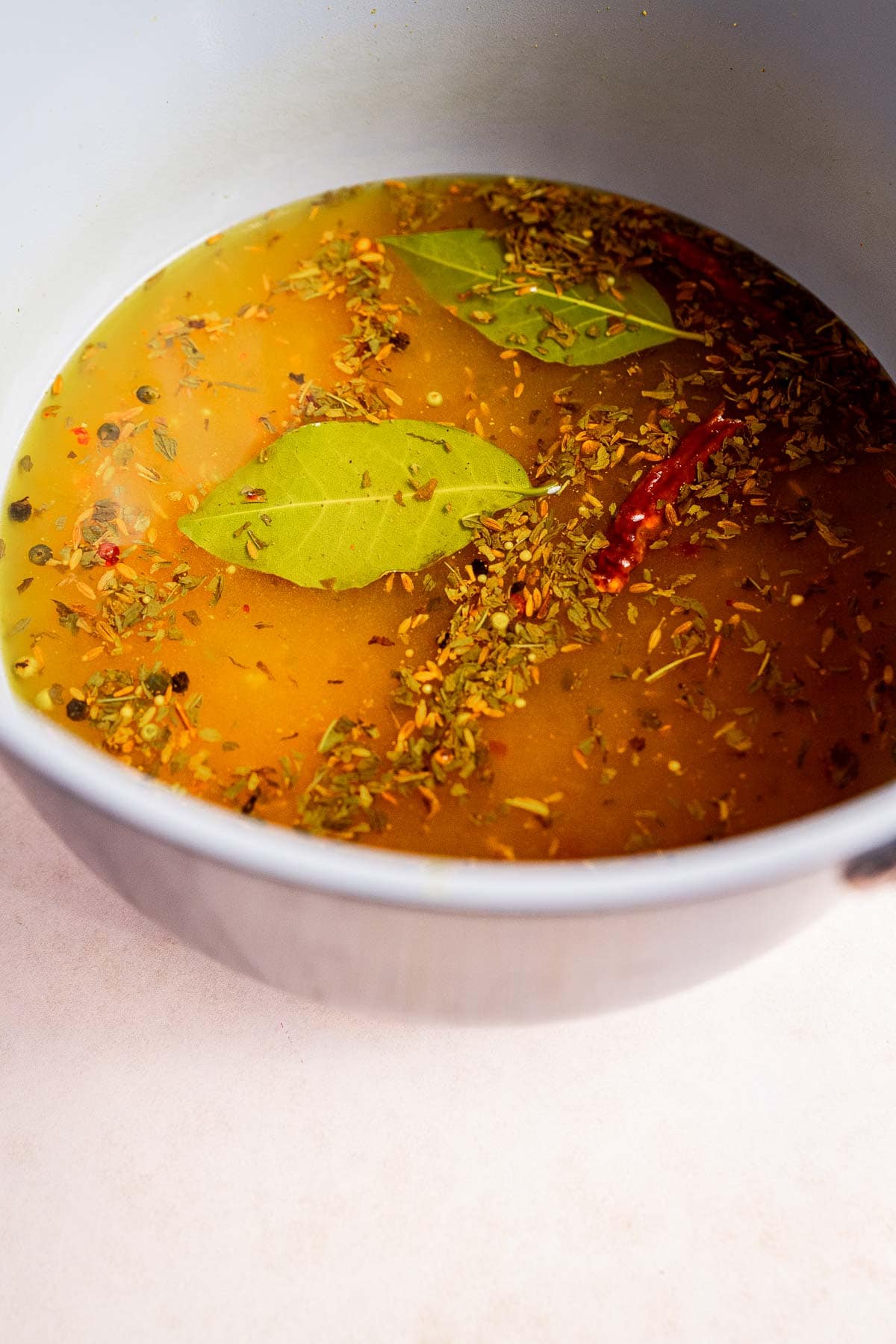 A pot containing seasoned broth with bay leaves, herbs, and spices—and a hint of torshi—floating on the surface.