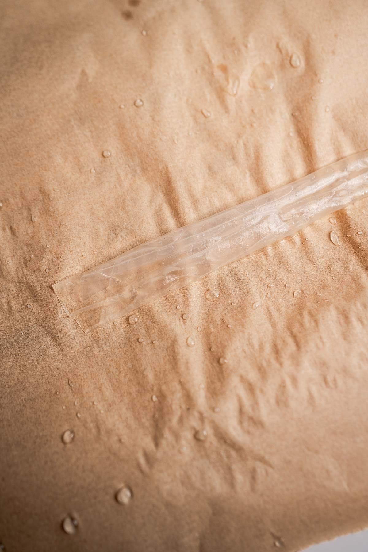 Close-up of a textured brown surface reminiscent of rice paper noodles, adorned with glistening water droplets and featuring a transparent strip or seal in the center.
