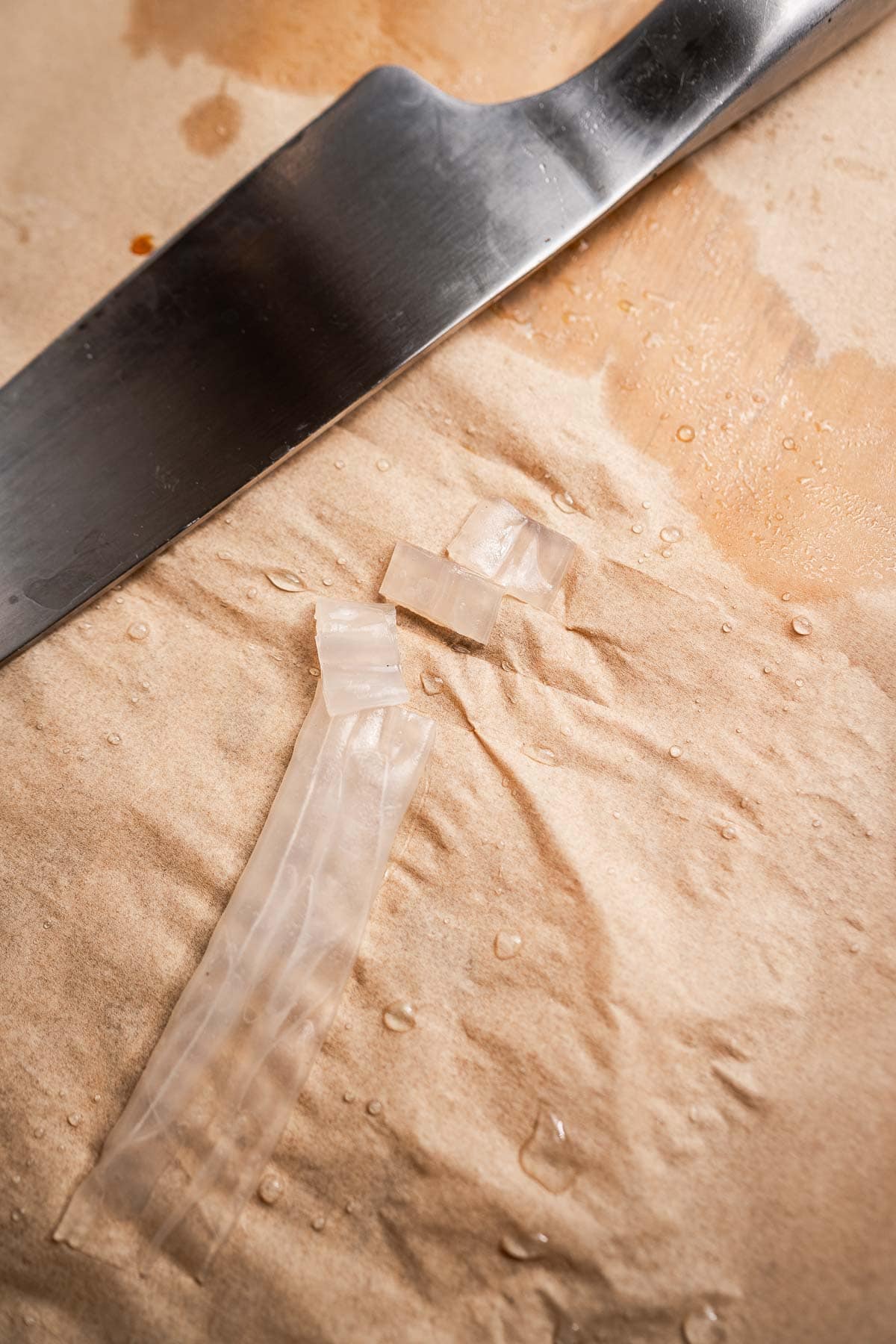 Knife on wet parchment with cut gelatin strips, resembling delicate rice paper noodles.