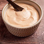 A bowl of creamy burrito sauce with a wooden spoon resting on a rustic wooden surface.