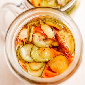 A jar filled with torshi, featuring sliced pickles and carrots in a flavorful brine.