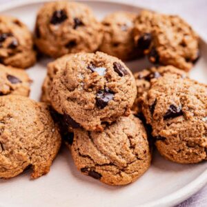 A plate of oat flour chocolate chip cookies rests on a white surface, showcasing a light brown texture with visible chocolate chunks.