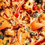 Close-up of a creamy vegetable stew featuring cauliflower, carrots, red bell peppers, and spinach in a rich, orange-colored sauce.