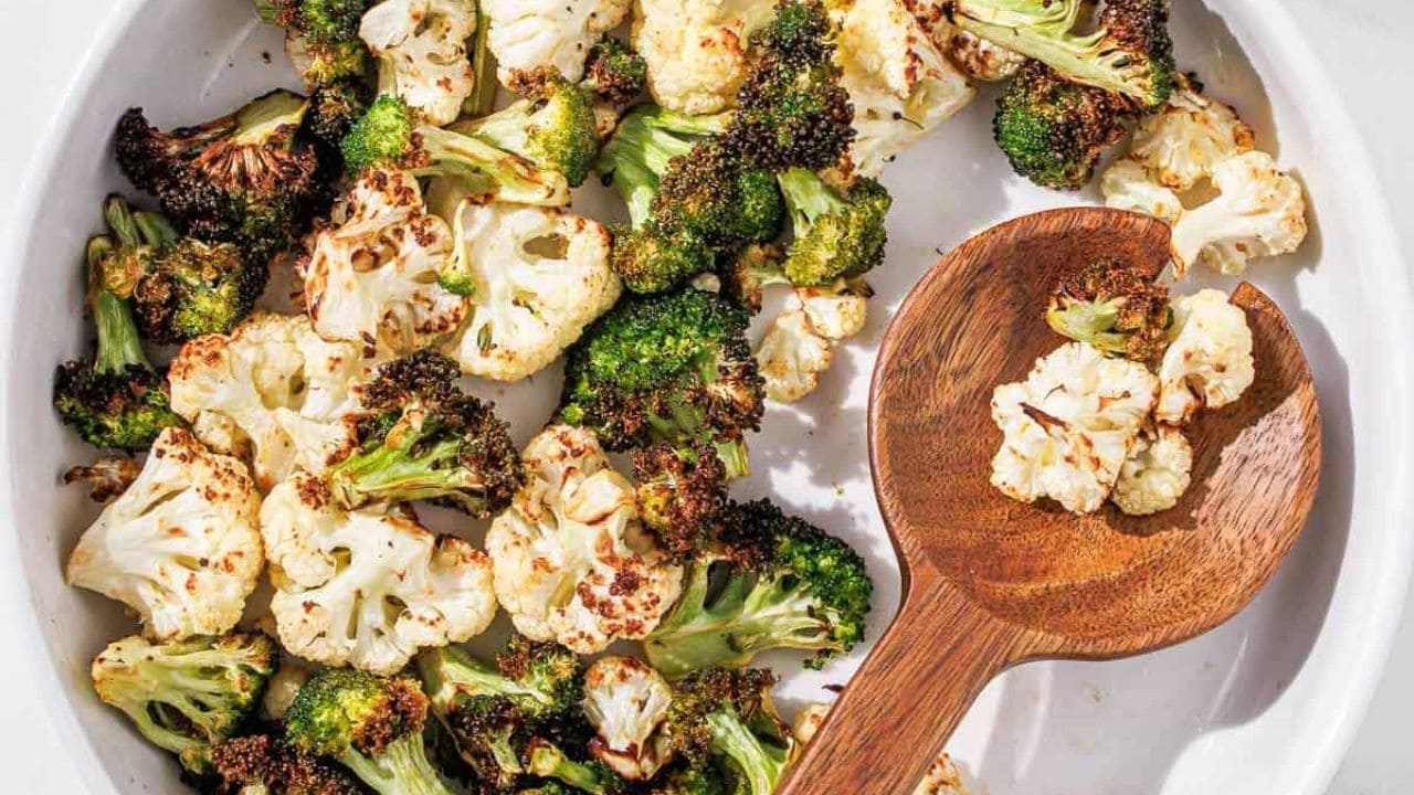 air fryer broccoli and cauliflower on a white plate with a pink linen and thyme.