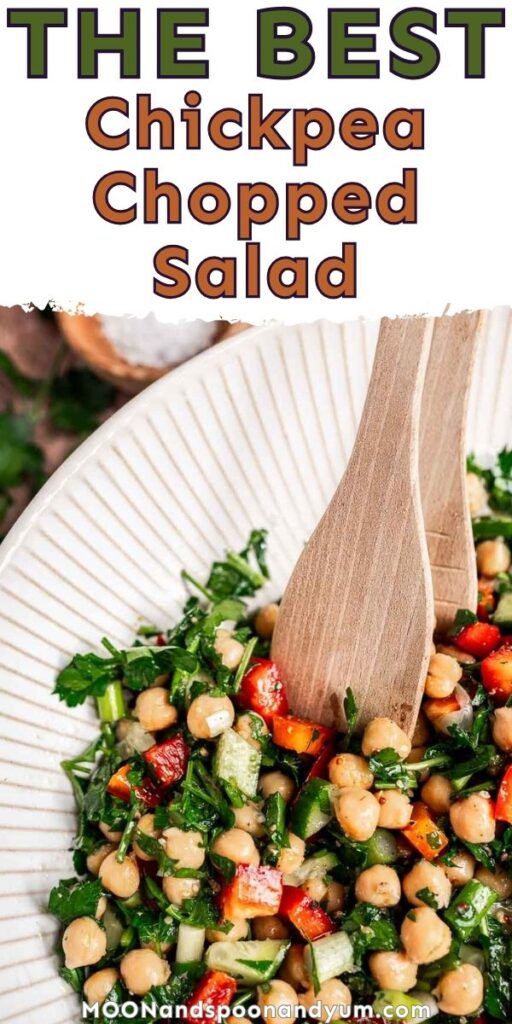 A bowl of chopped chickpea salad with cucumbers, red peppers, and herbs, served with wooden utensils.