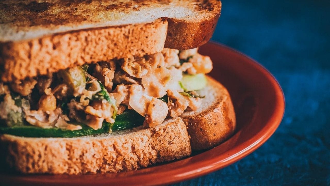 A sandwich with chickpea salad and cucumber slices between two toasted bread slices on a red plate.