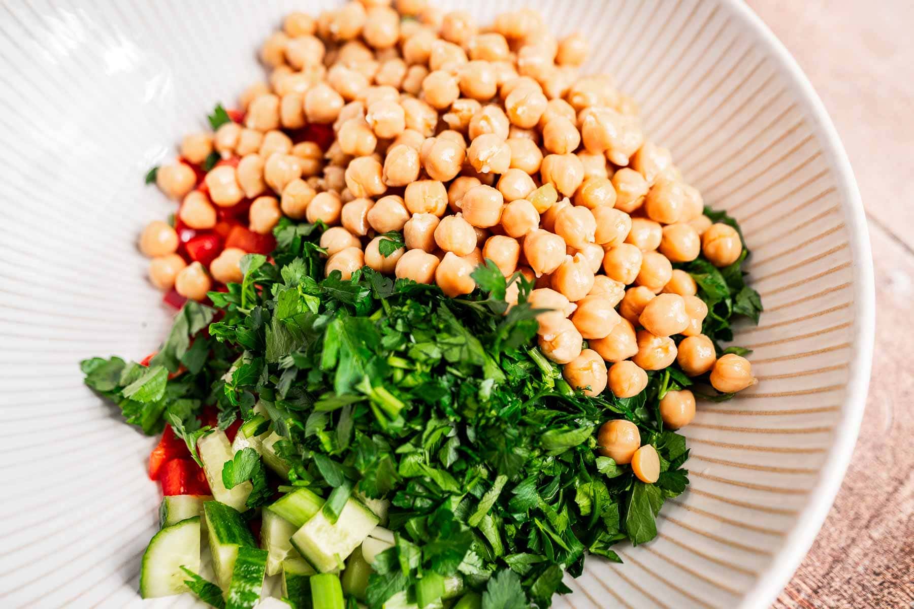 A refreshing chopped chickpea salad with chopped parsley, cucumber, and tomatoes elegantly served in a white bowl.