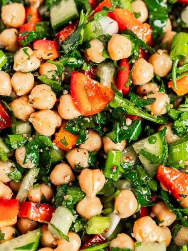 A close-up of a chickpea salad with chopped red peppers, cucumbers, parsley, and a light seasoning.