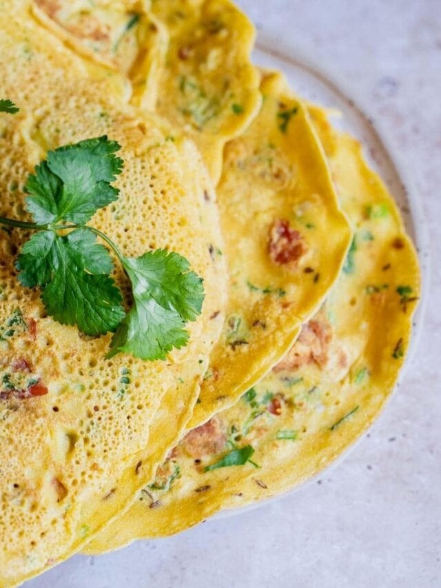 Yellow savory pancakes with herbs on top, garnished with a sprig of cilantro, placed on a white plate.
