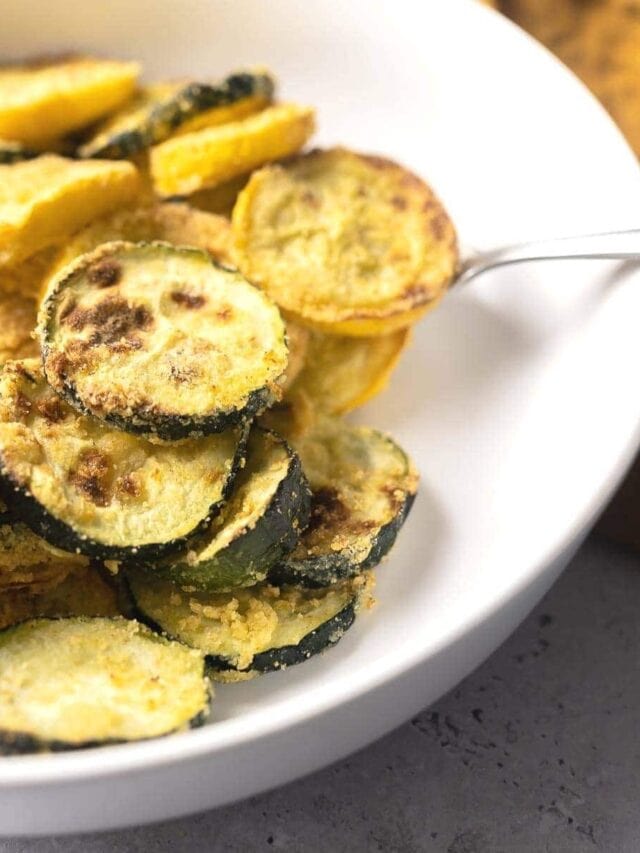 A white bowl filled with crispy, pan-fried zucchini slices. A metal spoon is partially visible, resting on the edge of the bowl.