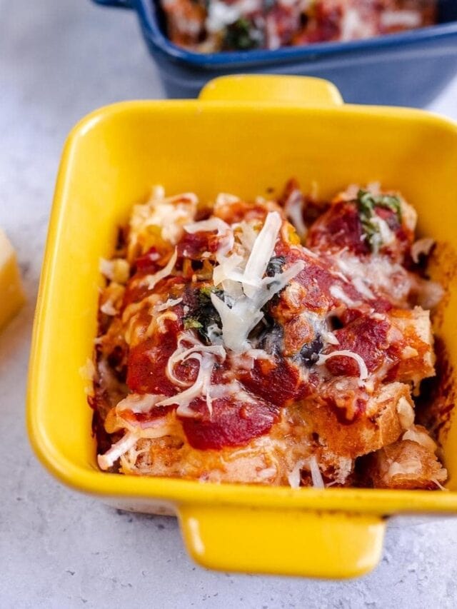 A yellow dish filled with baked bread pieces topped with tomato sauce, melted cheese, and spinach.