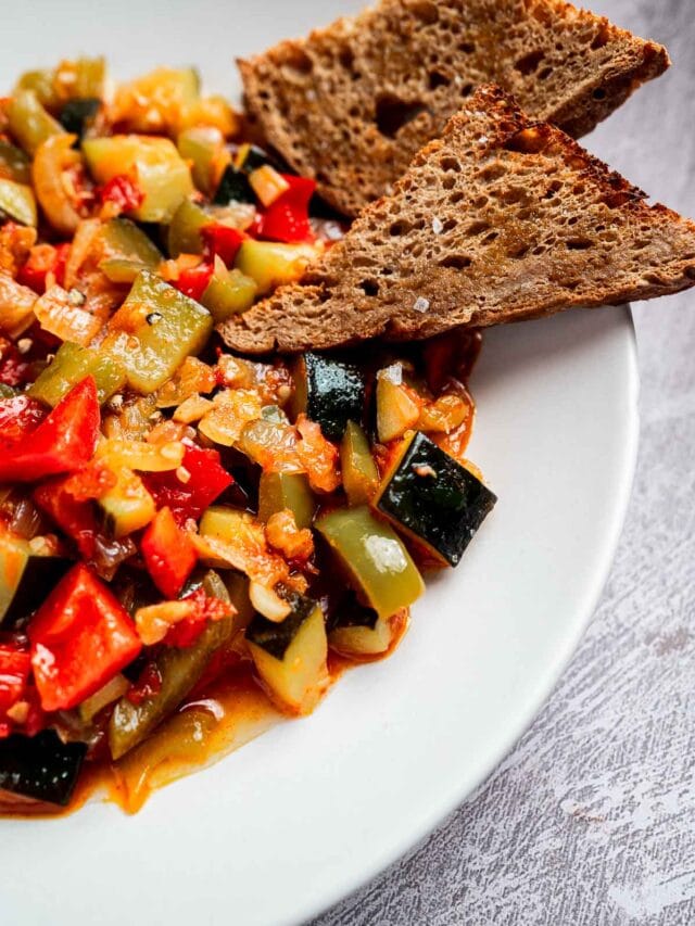 A plate of ratatouille with diced vegetables in sauce, accompanied by two slices of toasted bread on a white plate.