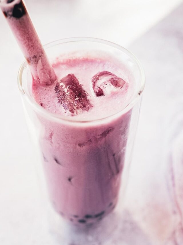 A tall glass of purple bubble tea with ice cubes and a wide straw, set against a light background.