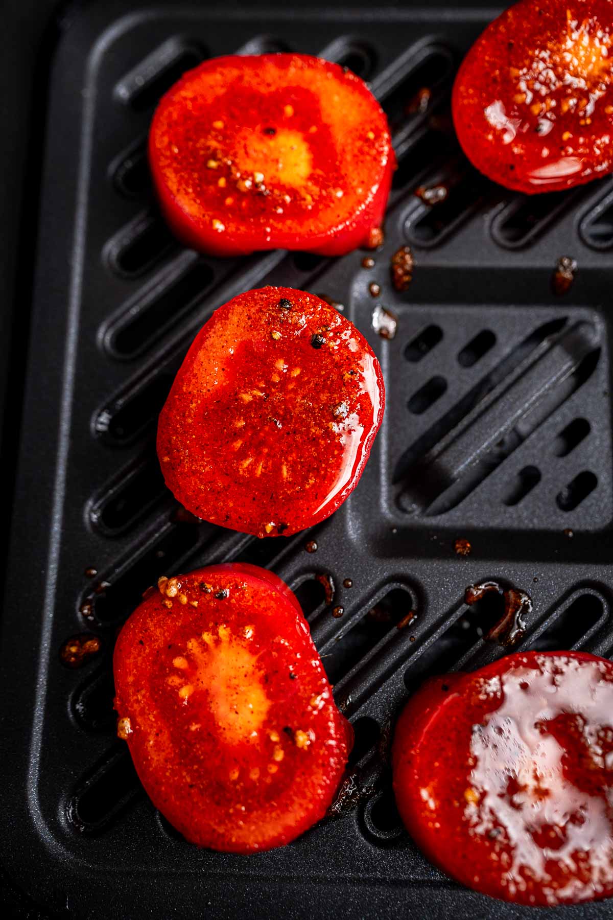 Sliced tomatoes seasoned with spices, glistening from heat as they cook to perfection in the air fryer.