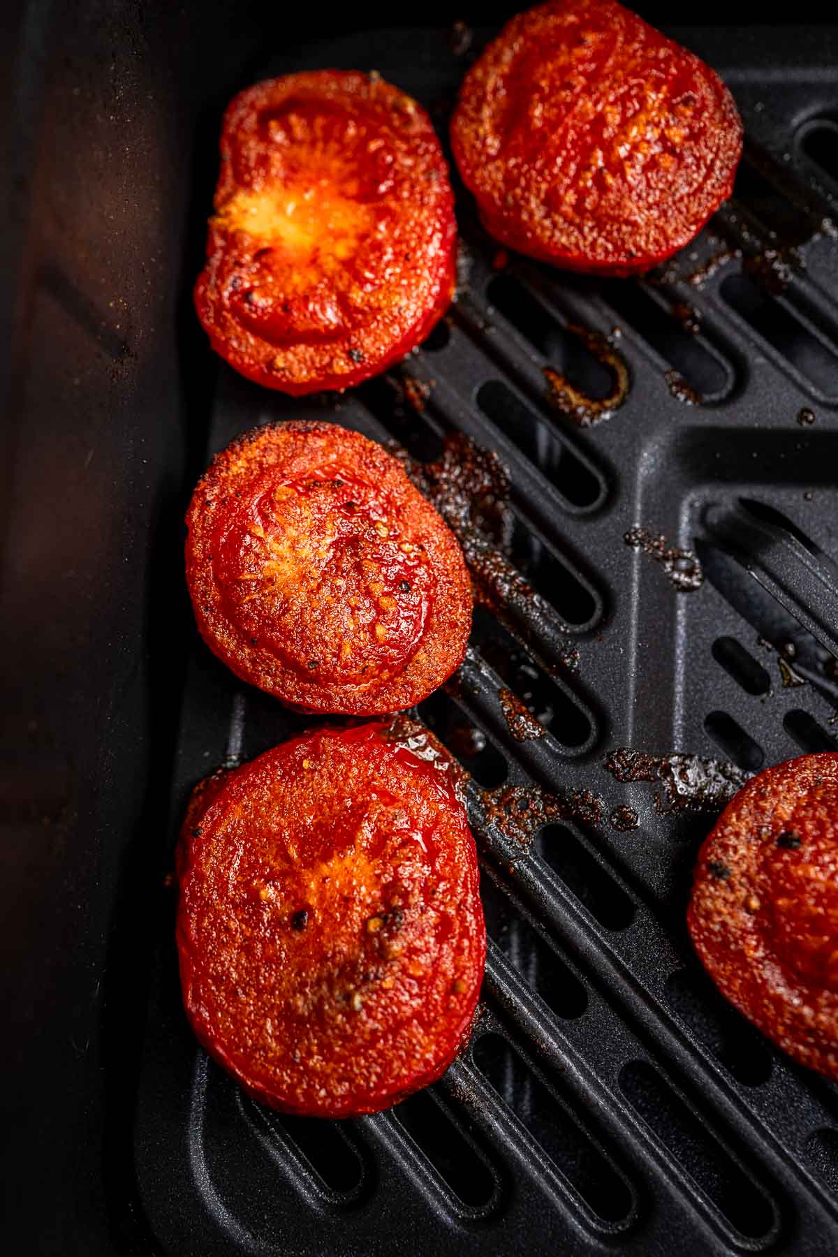 Slices of roasted tomatoes on a black griddle, effortlessly crafted to perfection, using the convenience of an air fryer.