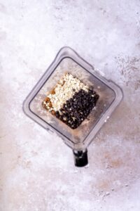 A top-down view of a blender containing oats, chocolate chips, and a light brown ingredient, all arranged in separate sections—perfect for making delicious black bean brownies.
