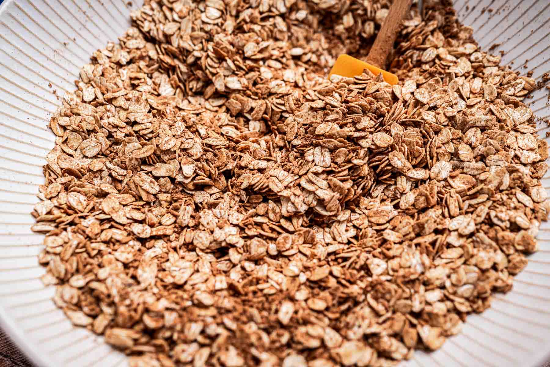 A bowl filled with granola, containing oats and seeds, with a small wooden scoop.
