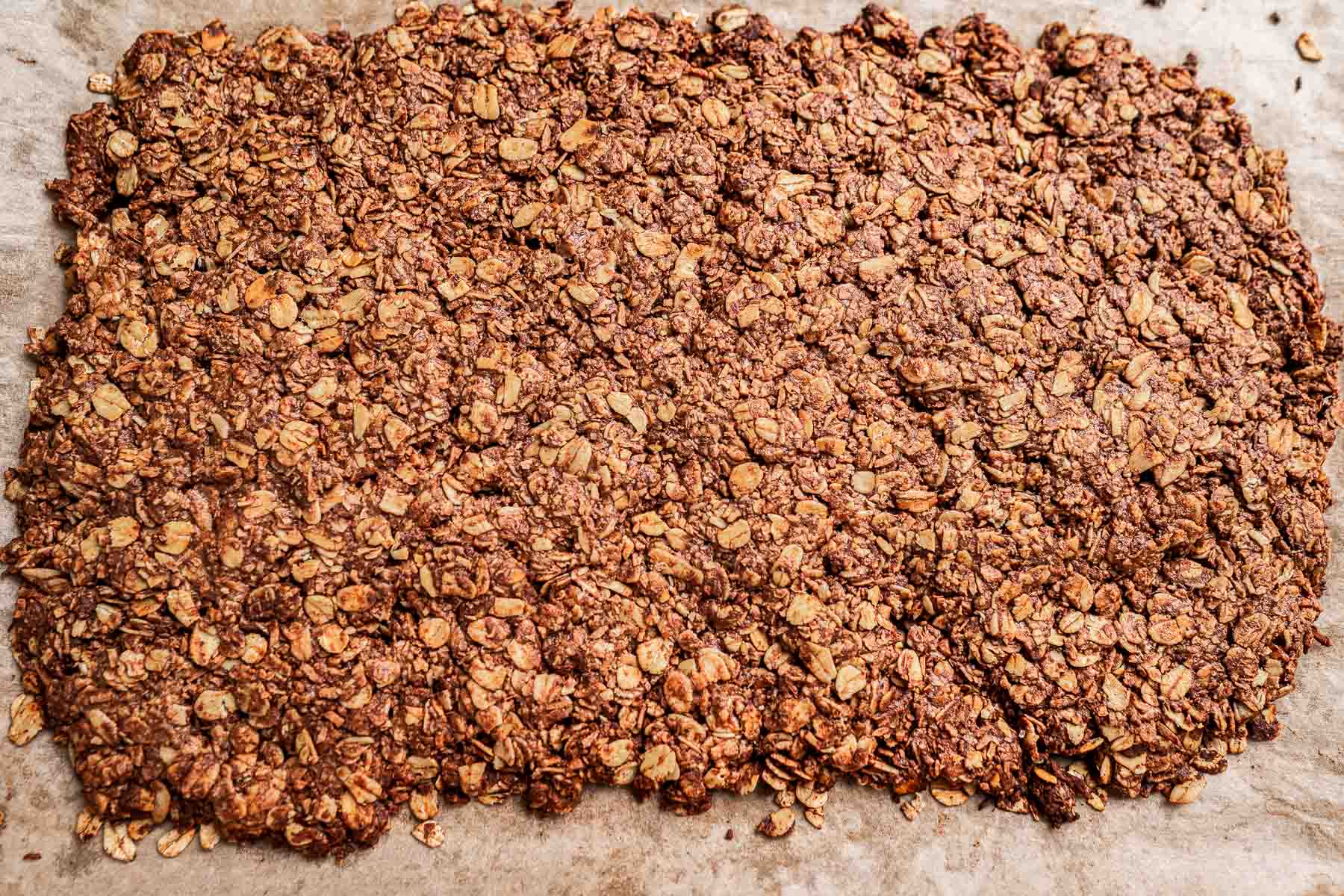 A large sheet of baked granola spread evenly on parchment paper.