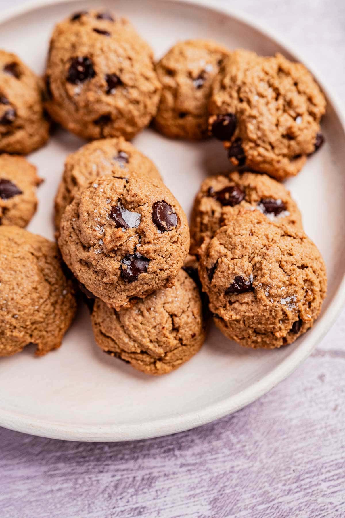 A plate of freshly baked oat flour chocolate chip cookies rests on a light surface.