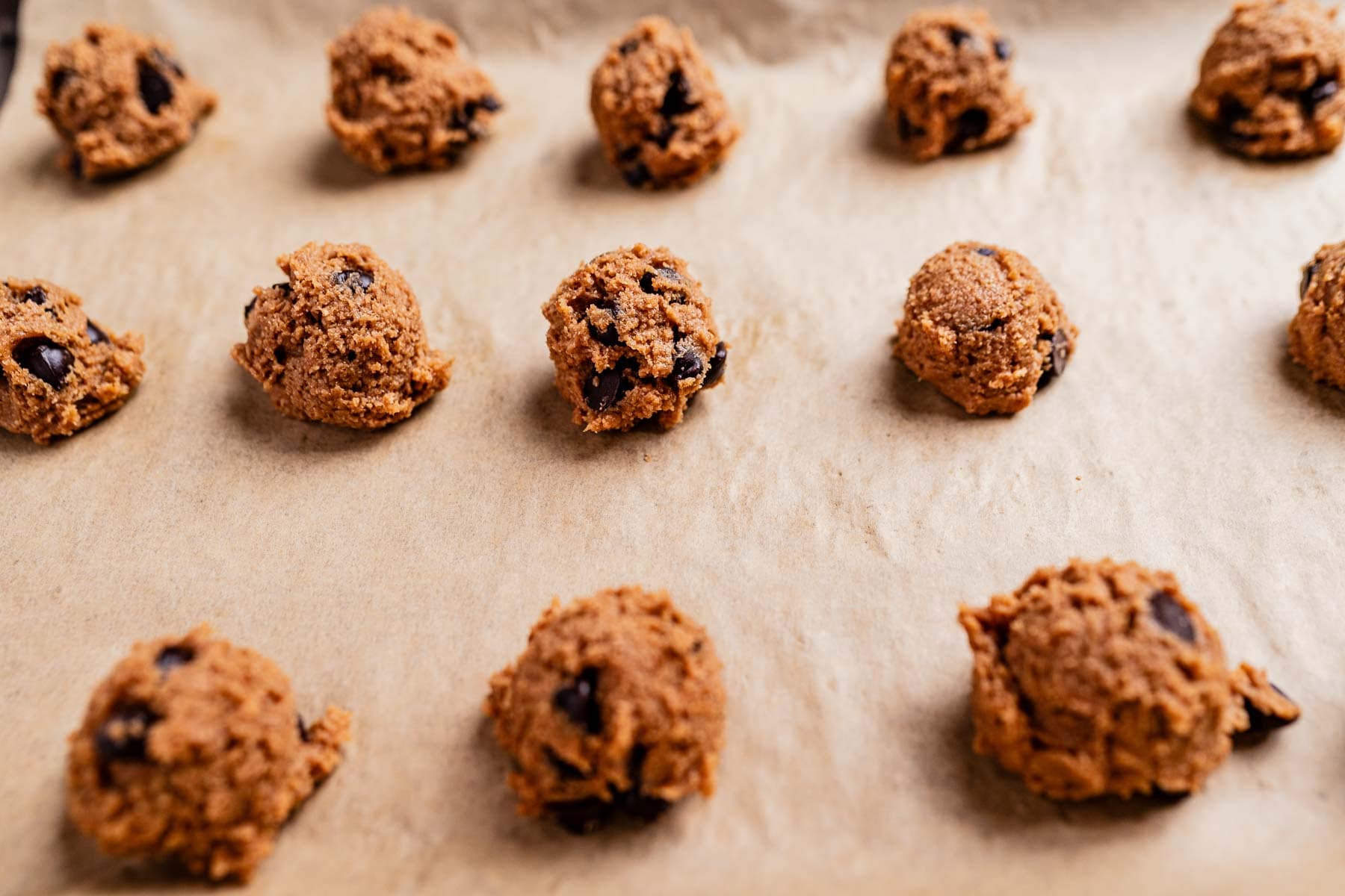 Raw oat flour chocolate chip cookie dough balls rest on a parchment-lined baking sheet, waiting to be baked into delicious perfection.